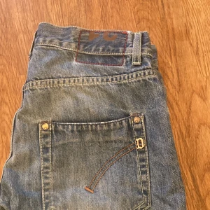 Blå jeans från Dondup, storlek 31 - Säljer ett par blå jeans från Dondup i storlek 31. Jeansen har klassisk femficksdesign, slitna detaljer och snygg tvätt med ljusare partier. Materialet är jeans med kontrastsömmar och metallnitar. Perfekta för dig som gillar en avslappnad och trendig look.