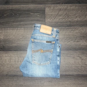 Nudie Jeans  - Snygga ljusblå skinny jeans från Nudie Jeans, modell Skinny Lin. Klassisk femficksdesign med orangea sömmar och Nudie-logga på bakfickan. Jeansen är i stretchig bomull och har en smal passform som sitter tight längs benen. JAG SKICKAR EJ FLER BILDER NÄR JAG BÄR JEANSEN! för storleksguide hänvisar jag till måtten och för bättre inblick i passformen rekommenderar jag att googla på modellnamnet. Jeansen kan vara uppsydda utan att jag noterat det så kolla måtten noggrant :)s3 midja 32cm, längd 100cm