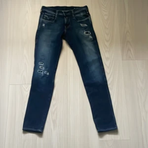 Replay Anbass jeans blå 28 - Snygga Replay Anbass jeans i mörkblå tvätt med slitningar och skinny fit. Klassisk femficksmodell med detaljerade bakfickor och tydliga slitningar framtill. Märkespatch bak i midjan. Perfekta för dig som gillar en smal siluett och coola detaljer.