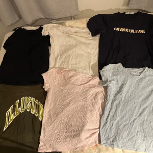 6-pack t-shirts - Säljer ett paket med sex t-shirts i olika färger och stilar. Två svarta, varav en med Calvin Klein Jeans-tryck och en med Illusion-tryck i gult. En vit, en ljusblå, en ljusrosa och en beige t-shirt. Alla har rund hals.