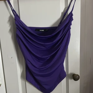 Lila omlott linnetopp från Bik Bok - Säljer en snygg lila linnetopp från Bik Bok i storlek XS. Toppen har tunna justerbara axelband och ett draperat omlott-framstycke som ger en cool och trendig look. Materialet är mjukt och har en lätt glansig finish som känns skönt mot huden. Använt på fester och utgångar ☺️den är skit snygg!!‼️