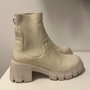 Beige chunky chelsea boots Steve Madden - Säljer ett par beige chunky chelsea boots från Steve Madden. Skorna har grov sula, rund tå och ribbade resårpaneler på sidorna. Använd 2 gånger