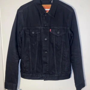 Svart jeansjacka från Levi's, S - Svart jeansjacka från Levi's i klassisk modell med raka linjer och krage. Materialet är slitstarkt denim och jackan har lång ärm. Passformen är regular. Jag är runt 175 lång och väger 67kg, jackan satt liten.