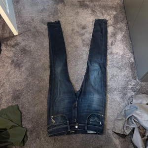 Replay Anbass slim fit  jeans mörkblå - Säljer ett par Replay Anbass jeans i mörkblå tvätt med snygga slitningar. Modellen är skinny fit med klassiska fem fickor och dragkedja. Jeansen har kontrastsömmar och är tillverkade i stretchig jeansbomull för en tajt och bekväm passform.