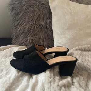 Svarta sandaler med klack från Shein - Säljer ett par svarta sandaler från Shein med bred rem över foten och öppen tå. Skorna har en rund tå och en stabil, hög klack. Materialet är mocka och innersulan är beige. Perfekta för dig som gillar stilrena och enkla skor med lite höjd.