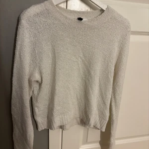 Vit stickad tröja från H&M Divided - Mysig vit stickad tröja från H&M Divided i storlek M. Tröjan har en enkel design med rund hals och långa ärmar. Materialet är fluffigt och ger en skön känsla, perfekt för kyliga dagar. Passformen är normal och muddar finns vid ärmslut och nederkant.