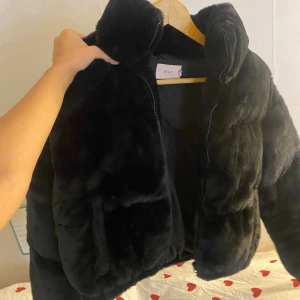 Svart pälsjacka från Nelly - Fluffig svart pälsjacka från Nelly med dragkedja framtill och hög krage. Jackan är kortare i modellen och har en oversized vibe. Perfekt för att hålla sig varm och snygg under kyliga dagar. Storlek 36 