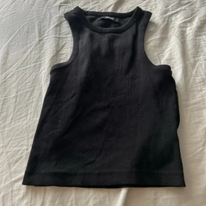 Svart ribbad linnetopp från BikBok - Säljer en svart ribbad linnetopp från BikBok i storlek M. Toppen är ärmlös med rund halsringning och har en tight passform. Perfekt att styla med jeans eller kjol för en clean look.