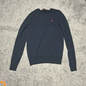 Mörkblå merinoullströja från Morris - Snygg mörkblå stickad tröja från Morris i 100% merinoull. Helt ny och oanvänd. Klassisk modell med röd logga på bröstet. Perfekt nu inför vintern då det blir kallare väder. Priset kan eventuellt diskuteras.