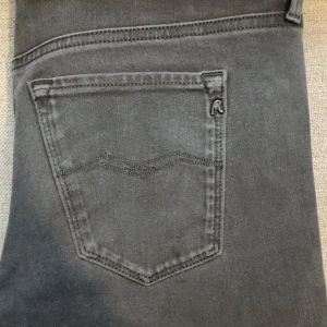 Replay Hyperflex svarta jeans W30 L30 - Svarta Replay Hyperflex jeans med klassisk femficksdesign och massa snygga detaljer. Jeansen har dragkedjegylf, Replay-logga på bakfickan och skinnpatch i midjan. Materialet är stretchigt och bekvämt, perfekt för en modern look. 