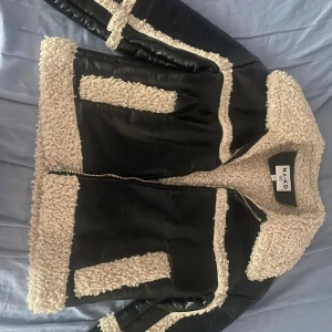 Svart teddyjacka från NA-KD med fuskpäls - Säljer en svart teddyjacka från NA-KD med krämvit fuskpäls på krage, ärmslut och längs kanterna. Jackan har dragkedja framtill och en oversized vibe. Perfekt för kalla dagar och riktigt snygg till jeans. Den är använt men har ingen synlig slitage, PERFEKT till vintern, väldigt varm. Säljer då jag köpt en ny liknande från nakd. Har två av samma jacka. 