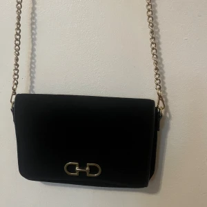 Svart axelväska med guldkedja - Snygg svart axelväska. Inte så använd men lite gammal, minns inte exakt från vart.