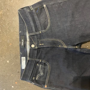Replay Anbass mörkblå jeans - Snygga mörkblå Replay Anbass jeans med kontrasterande gula sömmar och klassisk femficksdesign. Jeansen har raka ben och detaljerade bakfickor med broderad V-form. Perfekt passform och stilren look för dig som gillar kvalitetsjeans.                                                      W28 L32. Nypris ca 1700