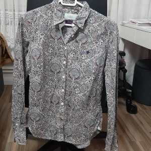 Mönstrad skjorta Morris Lady Liberty - Snygg skjorta från Morris Lady i samarbete med Liberty, storlek 36. Skjortan har ett detaljerat och färgstarkt mönster i blått, vinrött, beige och grått. Tillverkad i mjuk bomull med klassisk krage, knappar framtill och långa ärmar. Perfekt för dig som gillar unika prints.