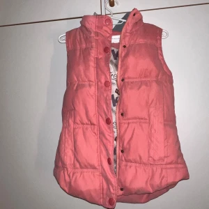 Rosa dunväst med huva från M.S.K.Z.X - Snygg rosa dunväst från M.S.K.Z.X med quiltad design och grå huva med snörning. Västen har dragkedja och knappar framtill samt två fickor. Perfekt för lager-på-lager och chill stil. Luvan går att ta bort om man önskar det 