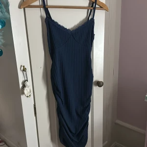Marinblå ribbad klänning med spets - Säljer en marinblå ribbad klänning med smala axelband och v-ringad spetskant upptill. Klänningen är figurnära och har snygg rynkdetalj längs sidan. Materialet känns stretchigt och bekvämt, perfekt för dig som gillar en stilren look med lite edge. Den här klänningen sätter sig perfekt längst din kropp och är så snygg‼️ Rekommenderar stek och om du frågar kan du få bilder när den klänningen sitter på mig 🥰 Andvänd 3 gånger förra året ☺️