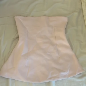 Ljusrosa korsettopp från Zara - Supersnygg ljusrosa korsettopp från Zara med figurnära passform och lätt utsvängd nederkant. Toppen är axelbandslös och har en stilren, minimalistisk look som passar perfekt till jeans eller kjol. Perfekt för dig som vill ha en trendig och feminin vibe.