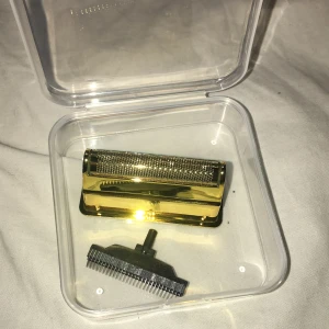 Guldfärgat rakapparatshuvud med trimmer  Kemei - Elegant guldfärgat rakapparatshuvud med tillhörande trimmerdel, levereras i plastförpackning. Passar till elektriska rakapparater. Produkten ser oanvänd ut och har inga synliga defekter eller slitage. Perfekt för dig som vill fräscha upp din rakapparat.