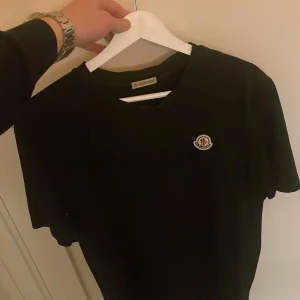 Svart Moncler t-shirt med logga - Säljer min moncler t shirt i storlek L då den är lite för stor. Den är helt äkta och köpt på nordiska kompaniet men säljer den billigt då den har 2 pytte små hål. Nypris ligger på runt 2500. Jag har kvitto och allting kvar så det är bara att skriva om ni vill ha fler bilder på tishan. 