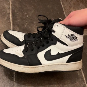 Nike Air Jordan 1 svart/vit high - Säljer ett par Nike Air Jordan 1 high sneakers i svart och vitt i storlek i storlek 38. Klassisk design med svart swoosh, snörning och perforerad tå. Tillverkade i skinn med högt skaft och ikonisk Air Jordan-logga på sidan.