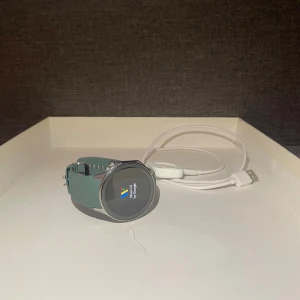 OnePlus 2 smartklocka med grön silikonrem - Snygg OnePlus smartklocka med rund urtavla, silverfärgad boett och grön silikonrem. Klockan kör Wear OS by Google och har en stilren, modern design. Perfekt för dig som gillar teknik och vill ha koll på notiser, hälsa och träning. Laddkabel medföljer.