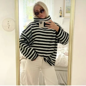 Randig svartvit oversized polotröja - Mysig oversized polotröja med breda svarta och vita ränder. Tröjan har hög krage och långa ärmar, perfekt för kyliga dagar. Den är fluffig och har en avslappnad passform som ger en cool och bekväm stil.