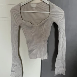 Beige ribbad långärmad topp H&M - Säljer en beige ribbad topp från H&M med lång ärm och snygg v-ringad urringning. Toppen har figurnära passform och markerade sömmar framtill som ger en modern look. Perfekt att styla med jeans eller kjol.