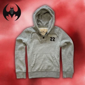 Grå hoodie från Hollister med tryck - Grå hoodie med tryck och broderat vitt Hollister-tryck och svart siffra 22 på bröstet | size M | längd: 65cm Axelbredd: 52cm Armlängd: 68cm | Passar för 170-185 cm