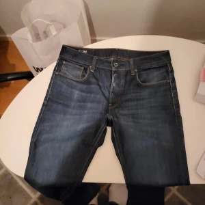 G-Star RAW 3301 Straight jeans blå W31 L32 - Säljer ett par G-Star RAW 3301 Straight jeans i mörkblå tvätt med klassisk femficksdesign och snygga kontrastsömmar. Modellen har rak passform och RAW-logga på både ficka och läderpatch bak. Perfekt för dig som gillar stilrena jeans med streetvibe.