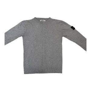 Grå stickad tröja från Stone Island - Snygg grå stickad tröja från Stone Island med klassisk rund hals och ribbade muddar. Tröjan har lång ärm och den ikoniska Stone Island-loggan på vänster ärm. Perfekt för dig som gillar stilrena och enkla plagg med en exklusiv touch. Pris kan diskuteras! Tröjan passar S 