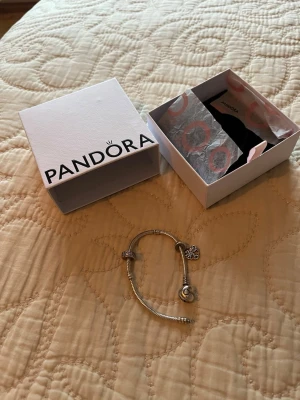 Pandora silverarmband med berlocker - Säljer ett snyggt Pandora-armband i silver med berlocker, bland annat ett hjärta med Pandora-logga och ett hängande berlock med trädmotiv. Armbandet har en klassisk design och kommer med original ask. Perfekt för dig som gillar personliga smycken. 16,5cm