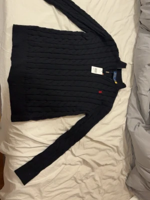 Svart stickad tröja Polo Ralph Lauren - Svart kabelstickad tröja från Polo Ralph Lauren i storlek XL. Tröjan har långärmad design, ribbade muddar och en liten röd broderad logga på bröstet. Perfekt för dig som gillar klassisk och stilren look med premiumkänsla. Pris kan även diskuteras vid en snabb affär. Är storlek XL men är ganska liten i storleken så den passar en med L
