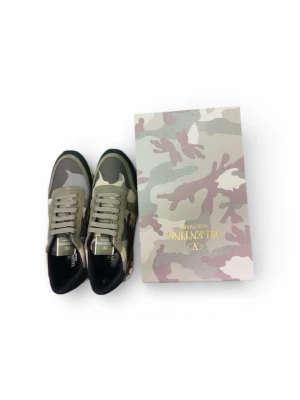 Valentino Rockrunner sneakers camo - Säljer ett par Valentino Rockrunner sneakers i camouflage med coola nitar på sulan. Skorna har en mix av mocka, mesh och skinn i gröna, beige och svarta toner. Klassisk snörning och rund tå. Perfekta för dig som vill sticka ut med en lyxig streetstyle.