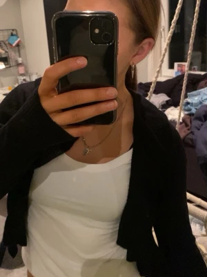 Svart croppad kofta med lång ärm - Säljer en svart croppad kofta med lång ärm och diskreta håldetaljer längs ärmarna. Koftan är stickad och har en enkel, stilren look som passar perfekt till jeans eller kjol. Den är lite kort men är väldigt snygg!!