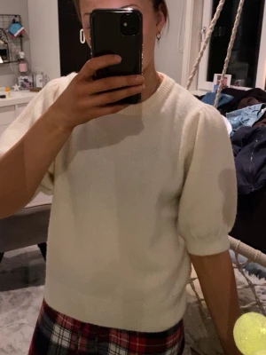 Vit stickad tröja med puffärm - Mysig vit stickad tröja med puffiga halvlånga ärmar och rund halsringning. Tröjan har en enkel och stilren design som passar perfekt till jeans eller kjol. Skön och mjuk känsla, perfekt för kyligare dagar.