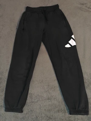 Svarta Adidas mjukisbyxor - Svarta mjukisbyxor från Adidas med stort vitt logotryck på benet och mindre logga vid mudden. Byxorna har snören i midjan, dragkedjefickor och muddar vid bensluten. Något baggy. Storlek XS men passar även S. Tydliga defekter och slitage finns vid höger ficka (bild 4) och på bakdelen (bild 5). Kontakta mig om du undrar något eller vill ha fler bilder. Pris kan alltid diskuteras! 🤝