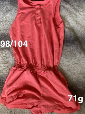 Rosa byxdress med knappar - Söt rosa byxdress med resår i midjan och tre knappar framtill. Ärmlös modell som passar perfekt till varma dagar. Enkel och bekväm att dra på sig.🌸 Fint använt skick. Storlek 98/104