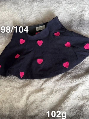 Marinblå kjol med rosa hjärtan H&M - Supersöt marinblå kjol från H&M med broderade rosa hjärtan över hela tyget. Kjolen har en klassisk kort modell. Perfekt för dig som gillar färgglada detaljer och lekfull stil.🌸 Fint använt skick. Storlek 98/104