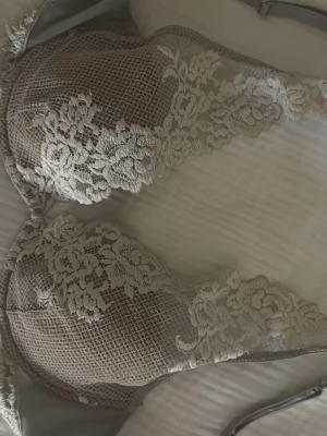 Intimissmi bh  - Säljer en snygg grå bh med tunna axelband och detaljerad spets i blommönster. Kuporna har en meshstruktur och spetsen går upp mot axelbanden för en extra fin look. Perfekt för dig som gillar stilrena underkläder med det lilla extra.
