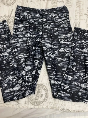 Svarta och vita mönstrade leggings - Säljer ett par snygga leggings med svart och vitt abstrakt mönster. De har hög midja och är tillverkade i ett stretchigt syntetmaterial som passar perfekt för träning eller chill. Tight passform som sitter skönt och följer kroppen.