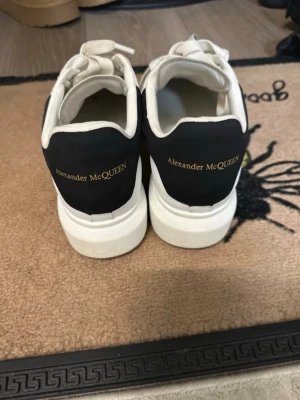 Vita Alexander McQueen sneakers - Säljer ett par klassiska vita sneakers från Alexander McQueen med svart häl och guldfärgad logga. Storlek är 41.