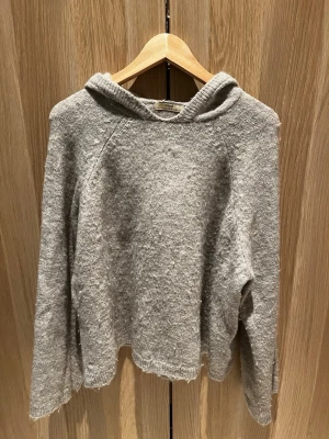 Grå stickad hoodie i ullmix - Mysig grå hoodie från Gina tricot premium i mjuk stickad ullmix. Tröjan har huva, lång ärm och relaxed fit. Perfekt för kyliga dagar och enkel att styla med jeans eller leggings.