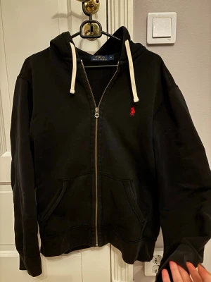 Svart polo kofta  - Säljer denna polo koftan då den inte används. Defekter finns och syns på bilderna i annonsen. Annars är den helt defektfri. Den är i storlek M men passar även S bra då den är lite tajtare 