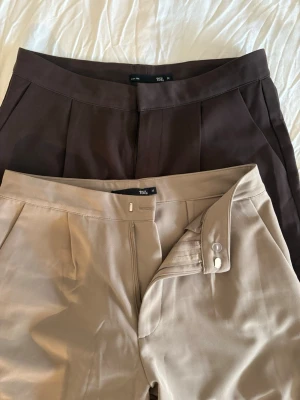 Två fina kostymbyxor  - Två klassiska kostymbyxor från Lager 157 👖 Ena paret i beige, det andra i brun. Knappt använda och i mycket fint skick – perfekt för jobb, fest eller vardaglig stil. Bekväm passform som sitter snyggt och stilrent.  ▫️ Märke: Lager 157 ▫️ Storlek: M ▫️ Skick: Knappt använda / mycket fint skick ▫️ Färger: Beige & Brun  Säljes tillsammans – perfekt baspaket för garderoben ✨ Hör av dig vid frågor eller intresse!