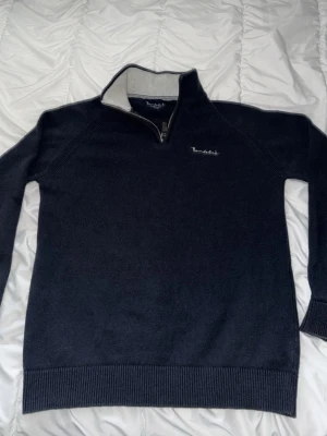 Mörkblå stickad tröja Bondelid half zip - Mörkblå stickad tröja från Bondelid med halv dragkedja och hög krage. Tröjan har diskret broderad logga på bröstet och kontrastfärgad insida i kragen. Perfekt för kyliga dagar och enkel att matcha med jeans.