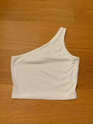 Vit one shoulder topp från SHEIN, storlek S - Säljer en vit ribbad one shoulder topp från SHEIN i storlek S. Toppen är ärmlös och har en asymmetrisk design med en axel. Materialet är mjukt och stretchigt, tillverkat av 65% bomull och 35% polyester. Perfekt för en trendig och stilren look.