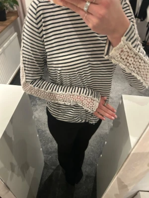 Randig långärmad topp med spets - Säljer en vit och svart randig långärmad topp med snygga spetsdetaljer längs ärmarna. Toppen har en avslappnad passform och är tillverkad i mjukt bomullsmaterial. Perfekt för dig som gillar en mix av klassiskt och romantiskt.