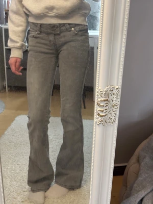 Grå bootcut jeans från Lager 157 - Säljer ett par gråa bootcut jeans från Lager 157 med snygg broderad detalj på bakfickorna. Jeansen har låg midja och klassisk femficksdesign. Dubbelknapp vid midjan.