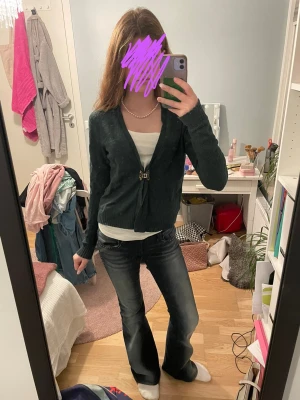 Mörkgrön kofta med dekorativ knäppning - Säljer en mörkgrön kofta med lång ärm och dekorativ knäppning framtill. Koftan har en smickrande v-ringning och är i ett mjukt stickat material. Perfekt att slänga över ett linne eller t-shirt för en snygg lager-på-lager-look.