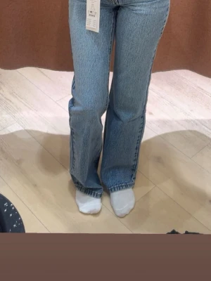 Blå raka jeans med hög midja - Säljer ett par klassiska blå jeans med hög midja och raka ben. Jeansen har fem fickor, bälteshällor och stängs med dragkedja och knapp. Materialet är robust denim i bomull och passformen är normal med en avslappnad vibe.